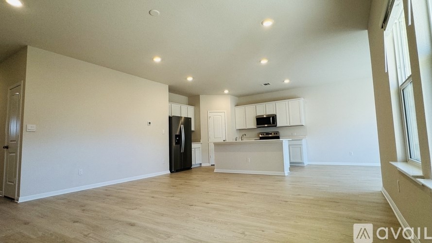 A spacious, empty room with wooden floors and a kitchen area in the background.