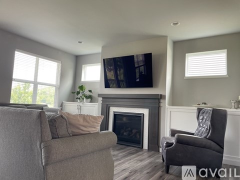 A living room with a grey couch, a grey armchair, a fireplace, and a television mounted on the wall.
