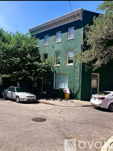 A white car is parked on the street in front of a green building.