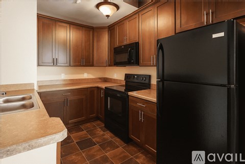 A kitchen with a black refrigerator and brown cabinets.