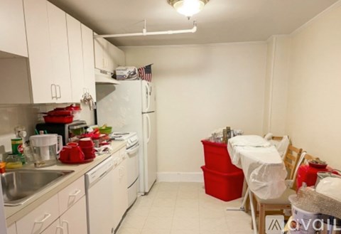 A kitchen with white cabinets and a white refrigerator with a red dish drainer and red chair.