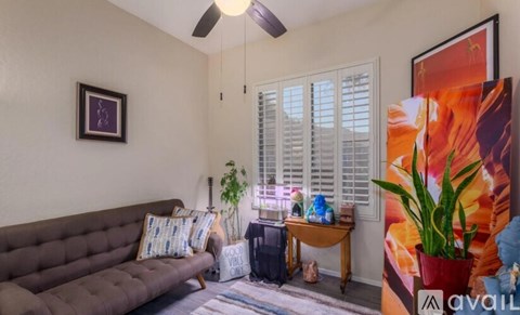 A living room with a brown sofa, a ceiling fan, and a painting on the wall.