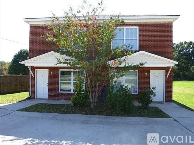 A red brick house with a white door and a tree in front.