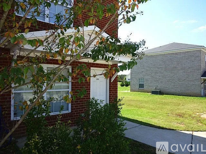 A house with a white door and windows is surrounded by greenery.