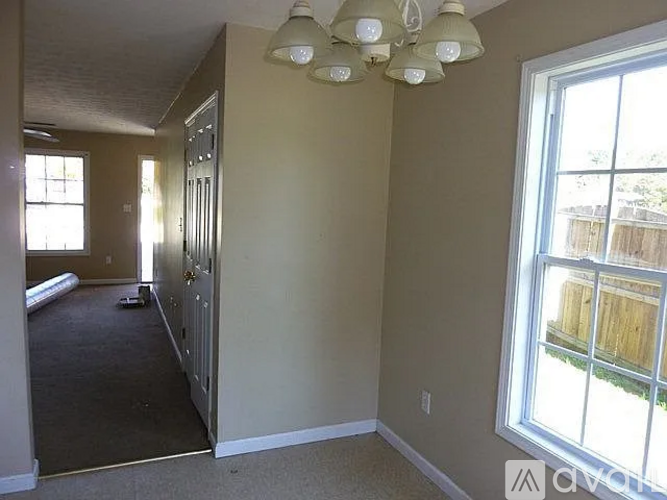 A room with a carpeted floor and a window showing a fence and trees outside.