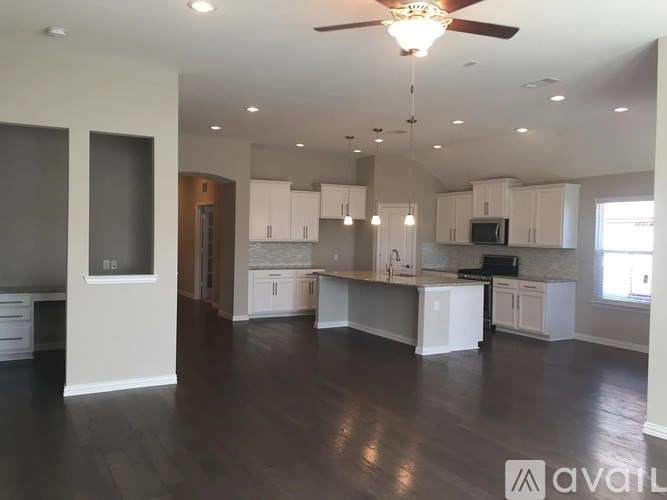 A spacious kitchen and living room with wood flooring and white cabinetry.