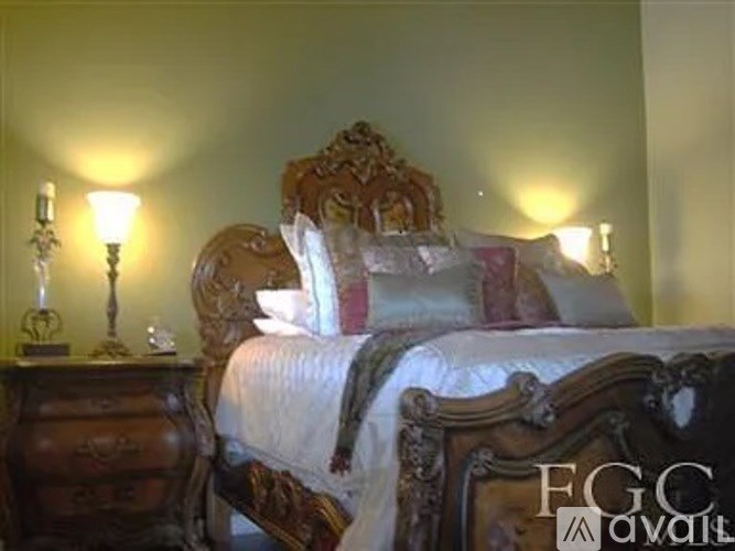 A bed with a wooden headboard and a white comforter sits in a room with two lamps on either side of the bed.