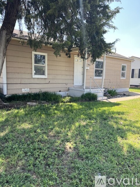 A beige house with a white door and windows is surrounded by green grass.