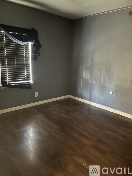 A room with wooden flooring and a window with blinds.