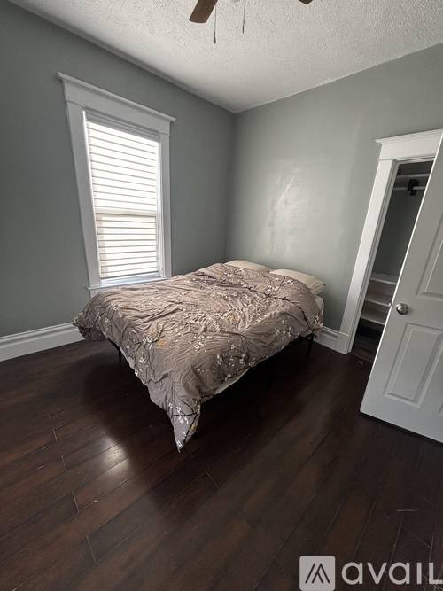 A bedroom with a bed, wooden floors, and a window with blinds.