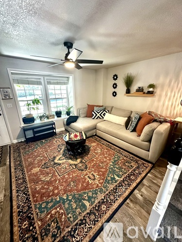 A living room with a rug, a couch, and a ceiling fan.