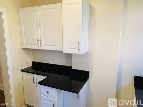 A kitchen with white cabinets and black countertops.