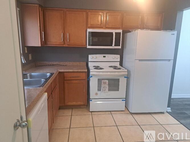 A kitchen with a white stove and refrigerator, wooden cabinets, and a tiled floor.