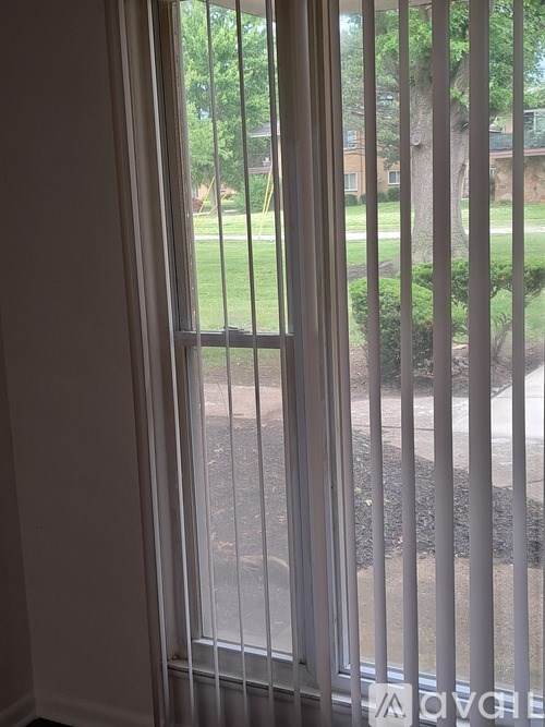 A view of a lawn through a window with blinds.