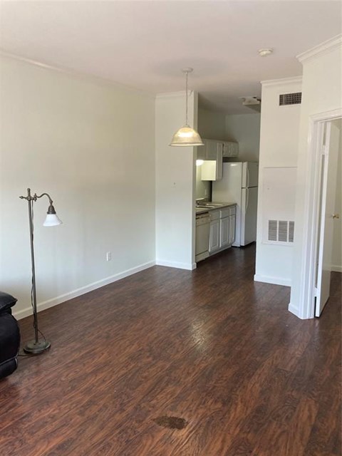 A room with wooden floors and a kitchen in the background.