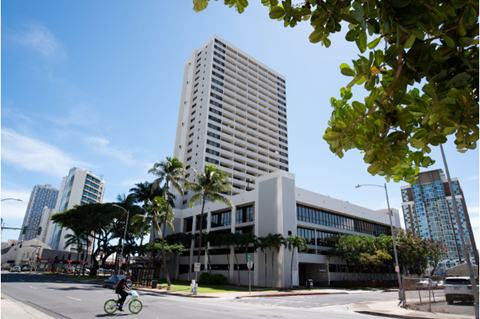 A tall white building with a lot of windows is in the middle of a street.
