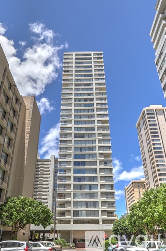 A tall building with many windows stands in the middle of a city street.