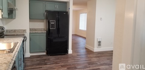 A black refrigerator in a kitchen with wooden floors.
