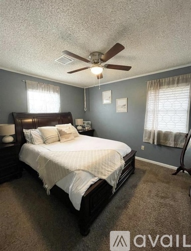 A bedroom with a bed, a ceiling fan, and a window with curtains.