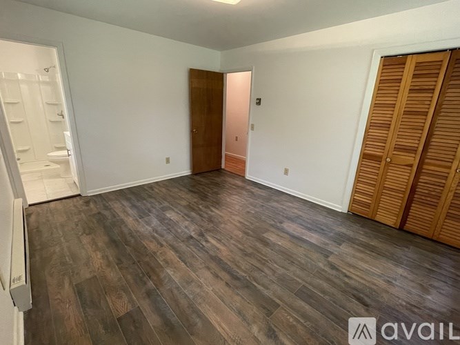 A room with wooden flooring and a white wall with a door and a window.