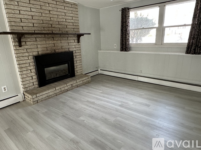 A room with a brick fireplace and wood flooring.