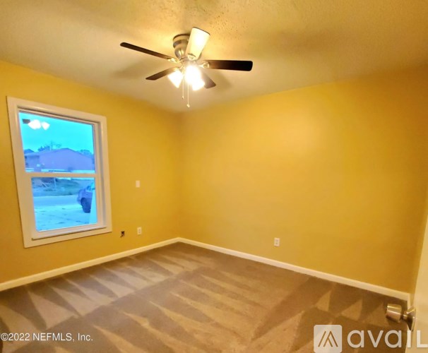 A room with a ceiling fan and a window showing an outdoor scene.
