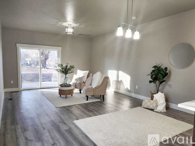A living room with a white rug, two chairs, a table with a plant, and a round mirror on the wall.