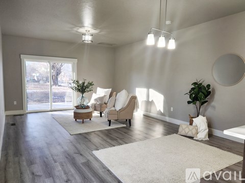 A living room with a white rug, two chairs, a table with a plant, and a round mirror on the wall.
