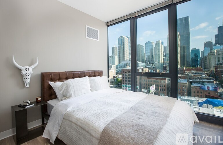 A bedroom with a large bed and a city view through the window.