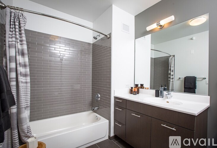 A bathroom with a white tub, sink, and grey tiles.