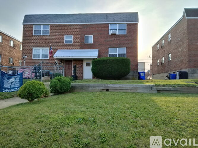 A red brick house with a white awning and a blue bin in front.