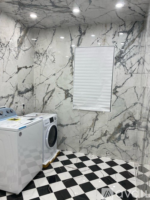 A white washing machine sits on a checkered floor in a marble bathroom.