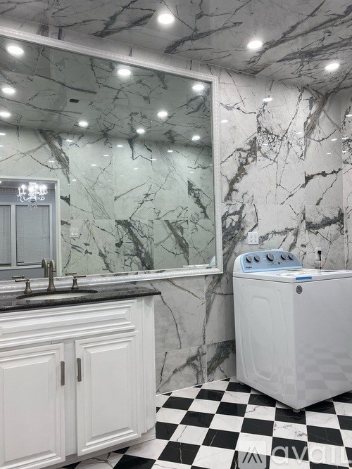 A white washing machine sits on a black and white checkered floor in a marble bathroom.