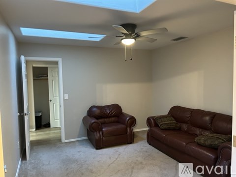 A living room with a brown leather couch and chair, a ceiling fan, and a skylight.