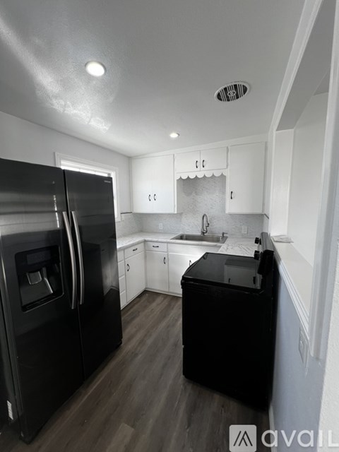 A black refrigerator stands in a kitchen with white cabinets and a wooden floor.