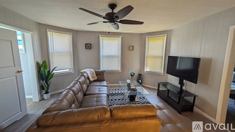 A living room with a brown leather couch and a ceiling fan.