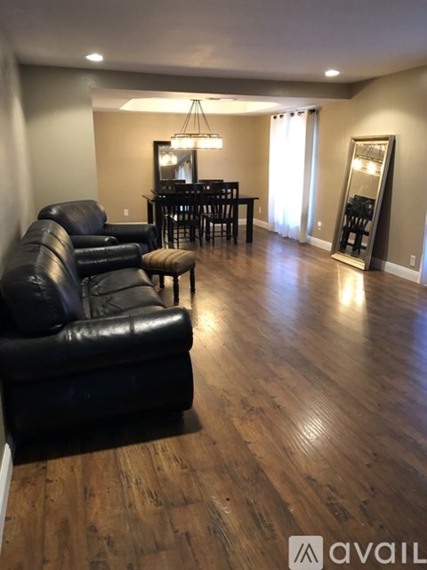 A living room with a black leather couch and a wooden floor.