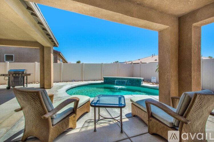 A pool surrounded by a wooden fence and a patio with chairs.