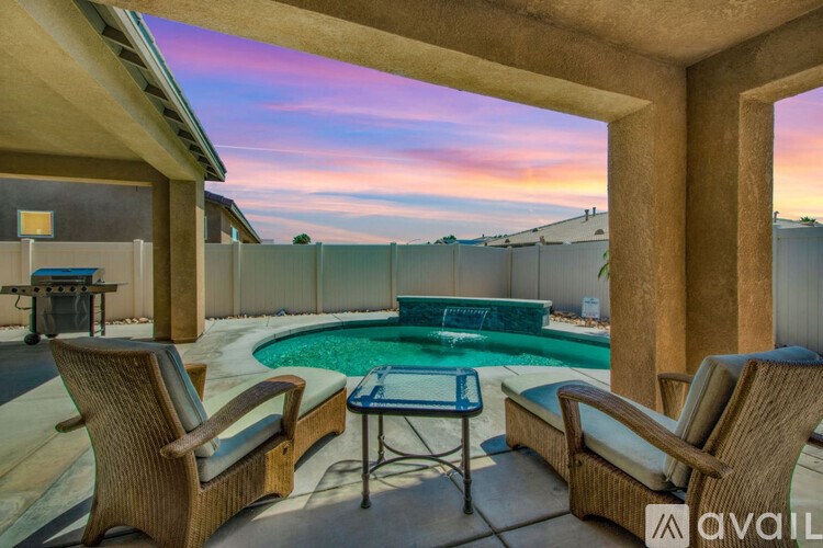 A pool surrounded by a fence with a sun lounger and table.