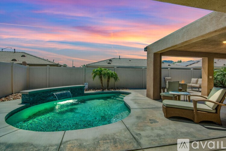 A pool with a waterfall and a patio area with chairs and a table.