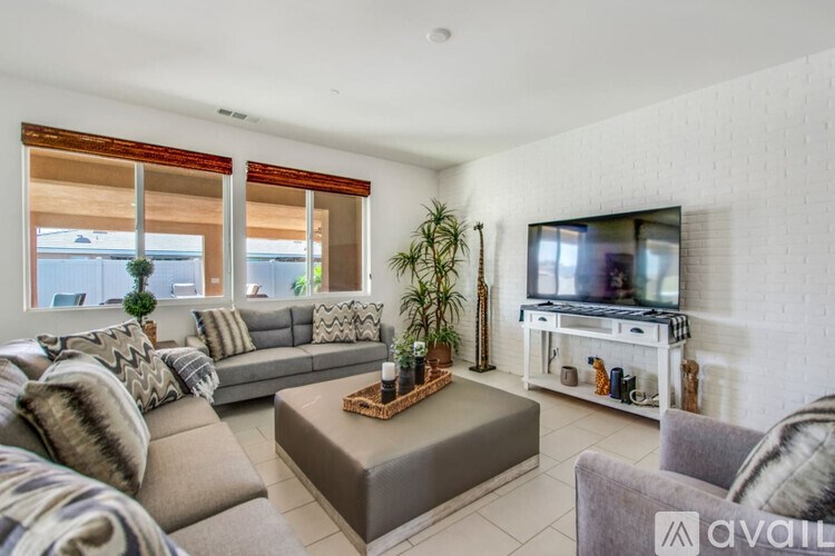 A living room with a grey sofa, a brown ottoman, and a television on a white stand.