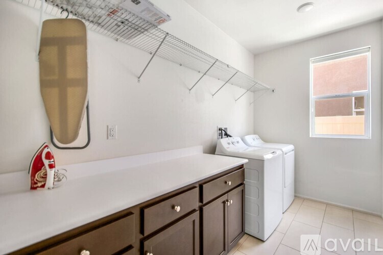 A laundry room with a washer and dryer, ironing board, and cabinets.