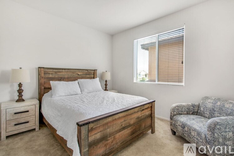 A bedroom with a large bed, a nightstand, a chair, and a window with blinds.
