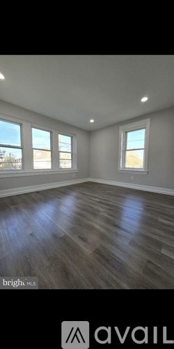 A spacious room with wooden flooring and three windows.