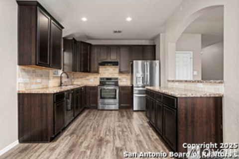 A kitchen with dark wood cabinets and a stainless steel refrigerator.