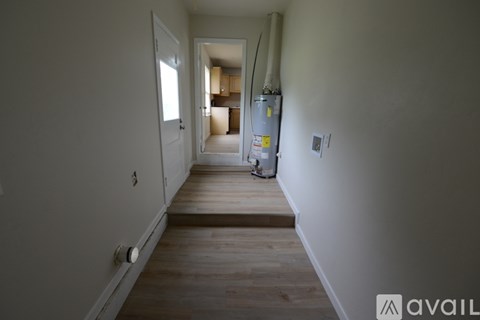 A long hallway with a door on the left and a kitchen in the distance.