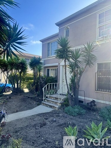 A house with a blue car parked in front and a tree in front of the house.