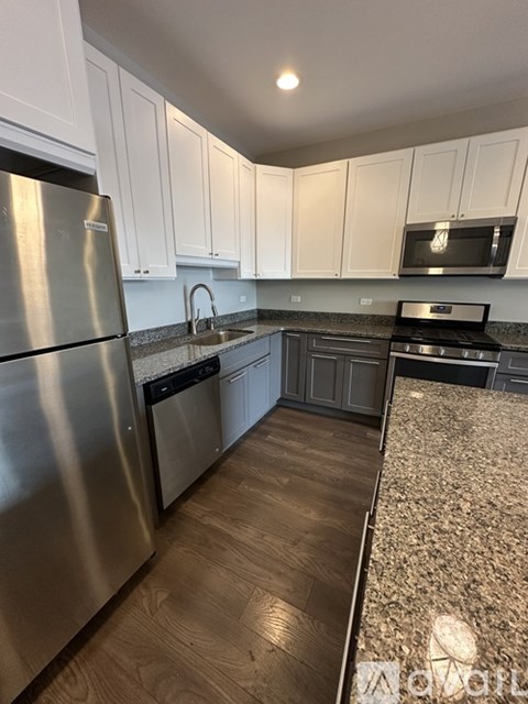 A kitchen with a stainless steel refrigerator and wooden flooring.
