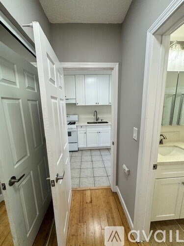 A small white kitchen with wood floors and a white door.