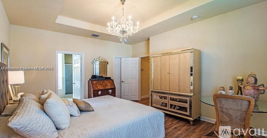 A bedroom with a large bed, a chandelier, and a wooden cabinet.